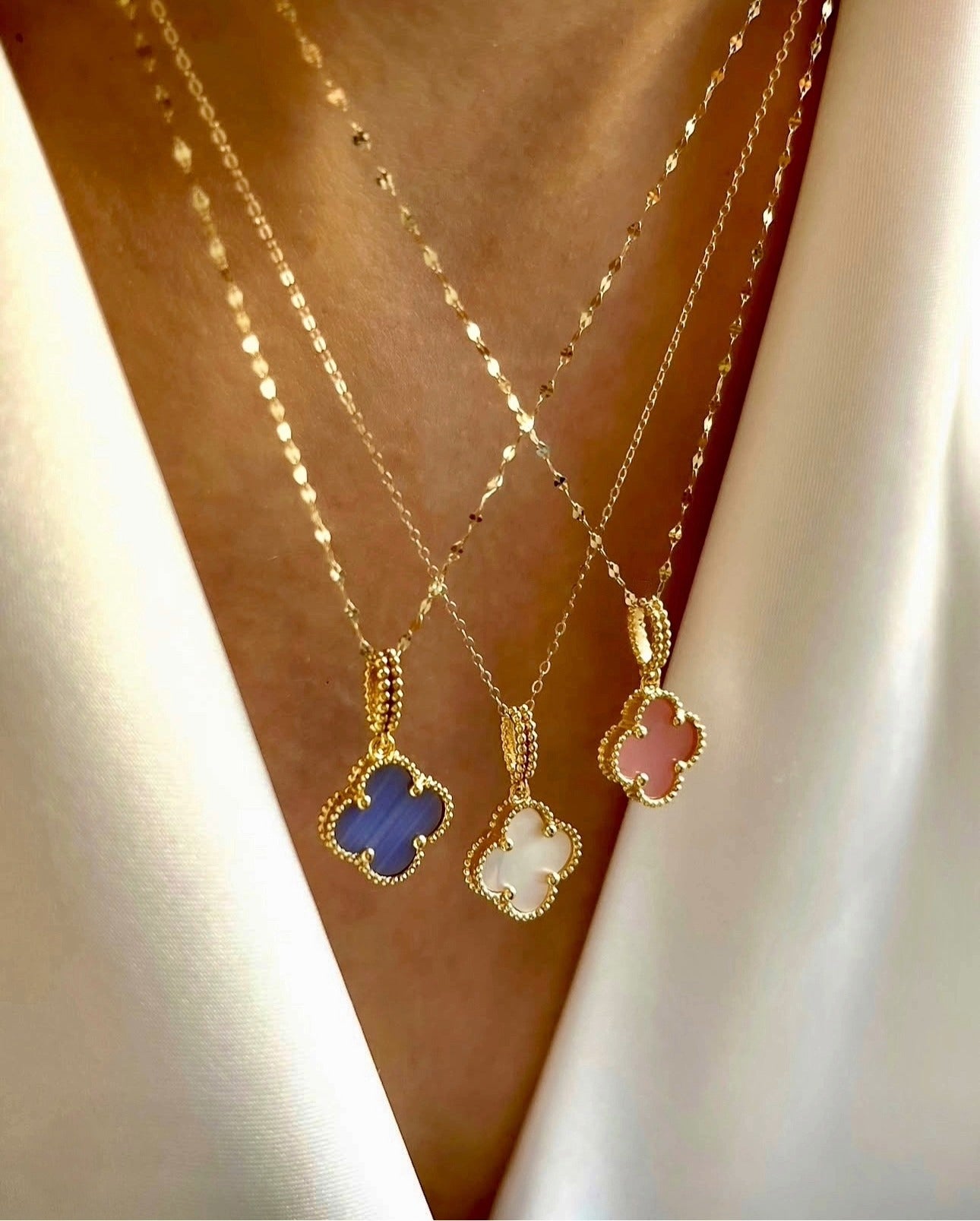 Anhänger in vierblättriger Form aus rosa Stein, eingefasst in feine goldene Perlenfassung, an einer zarten Goldkette, elegant auf heller Stoffbluse getragen.