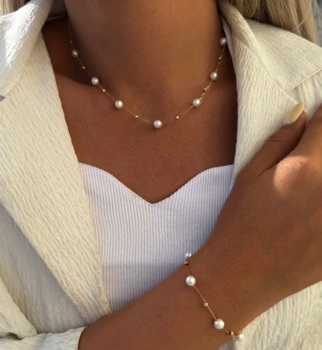 filigrane Kette mit eingearbeiteten weißen Perlen, elegant am Handgelenk getragen.