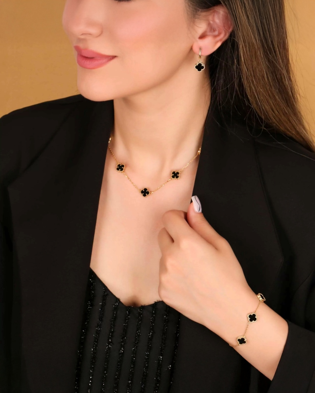 Frau trägt ein elegantes Schmuckset aus 18 Karat Gelbgold mit schwarzen Kleeblatt-Elementen – bestehend aus Halskette, Armband und Ohrringen. Der Look ist edel und modern, kombiniert mit einem schwarzen Outfit.
