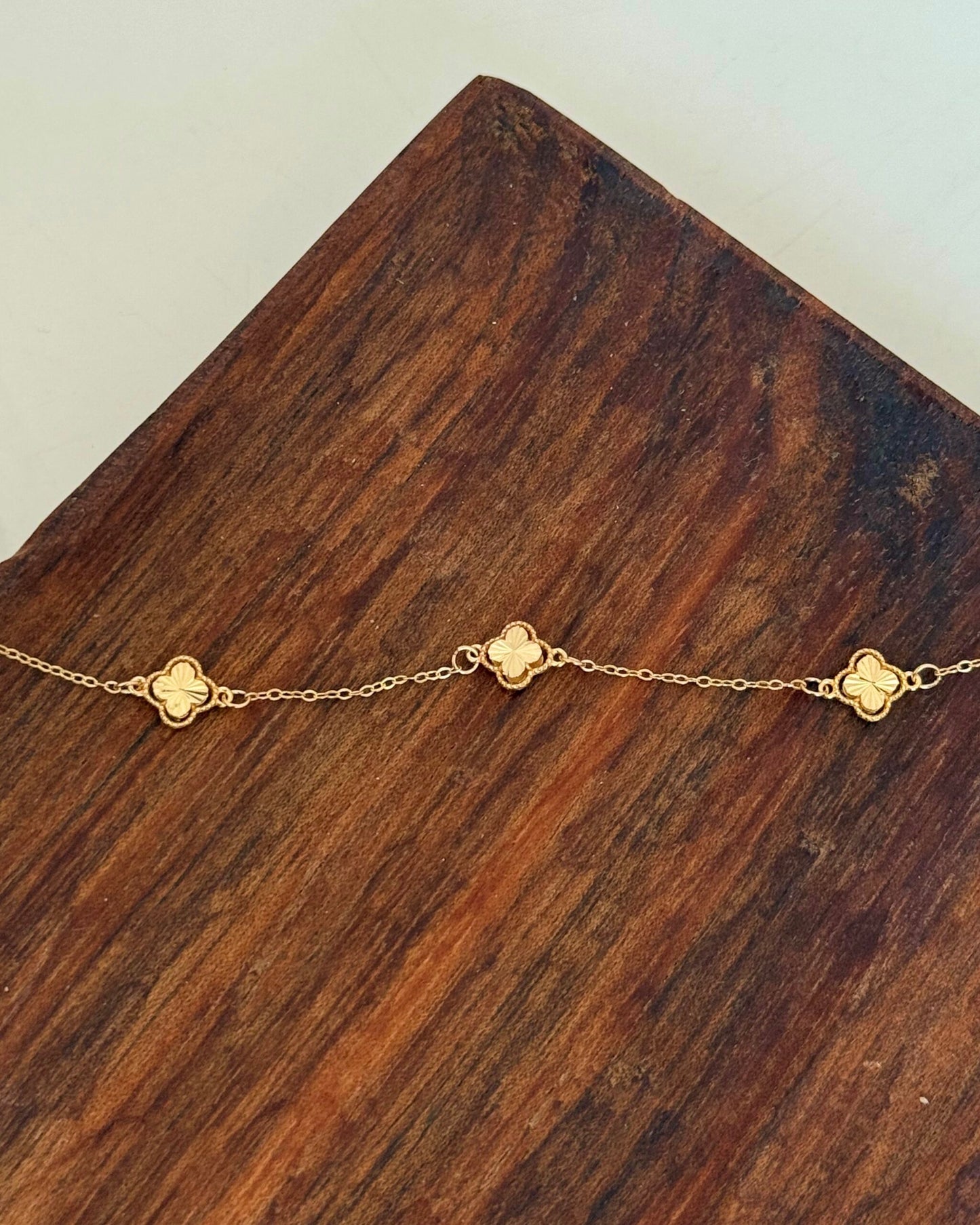 Feines Armband aus 18 Karat Gelbgold mit filigraner Kette und kleinen Kleeblatt-Elementen, die regelmässig entlang des Armbands eingearbeitet sind, dekorativ auf einer Holzoberfläche platziert.