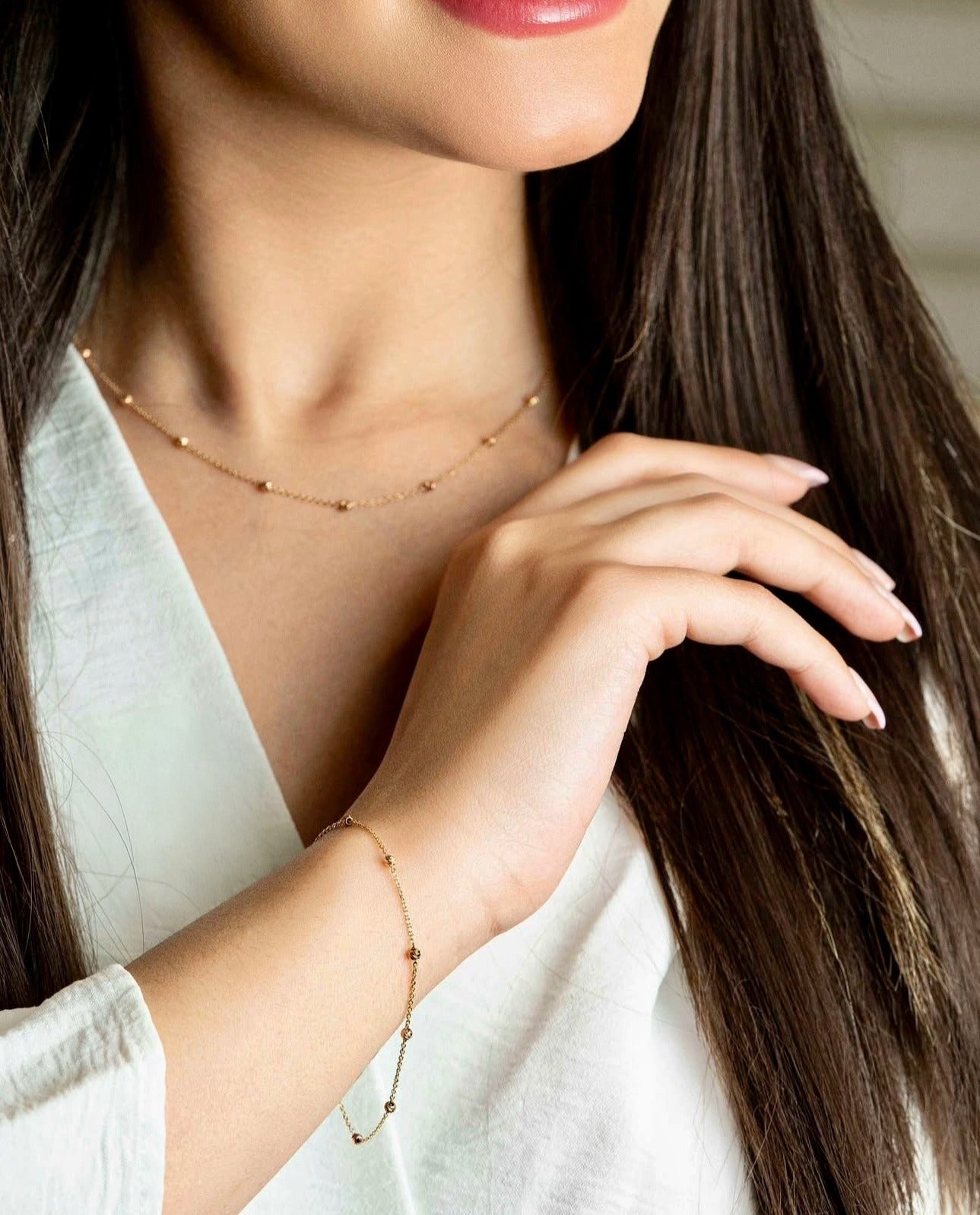 feine Kette mit dezenten Goldkügelchen, getragen am Handgelenk, elegantes und minimalistisches Schmuckdesign im Set mit passender Halskette.