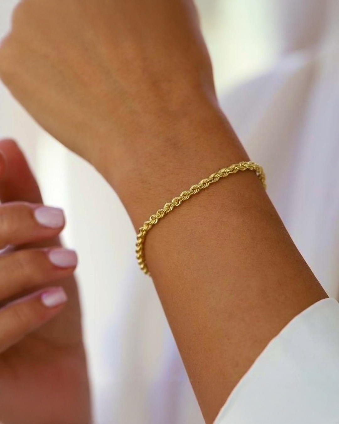 Feines Armband aus 18k Gelbgold in gedrehter Seiloptik, getragen am Handgelenk einer Frau mit heller Bluse – Detailaufnahme bei natürlichem Licht.
