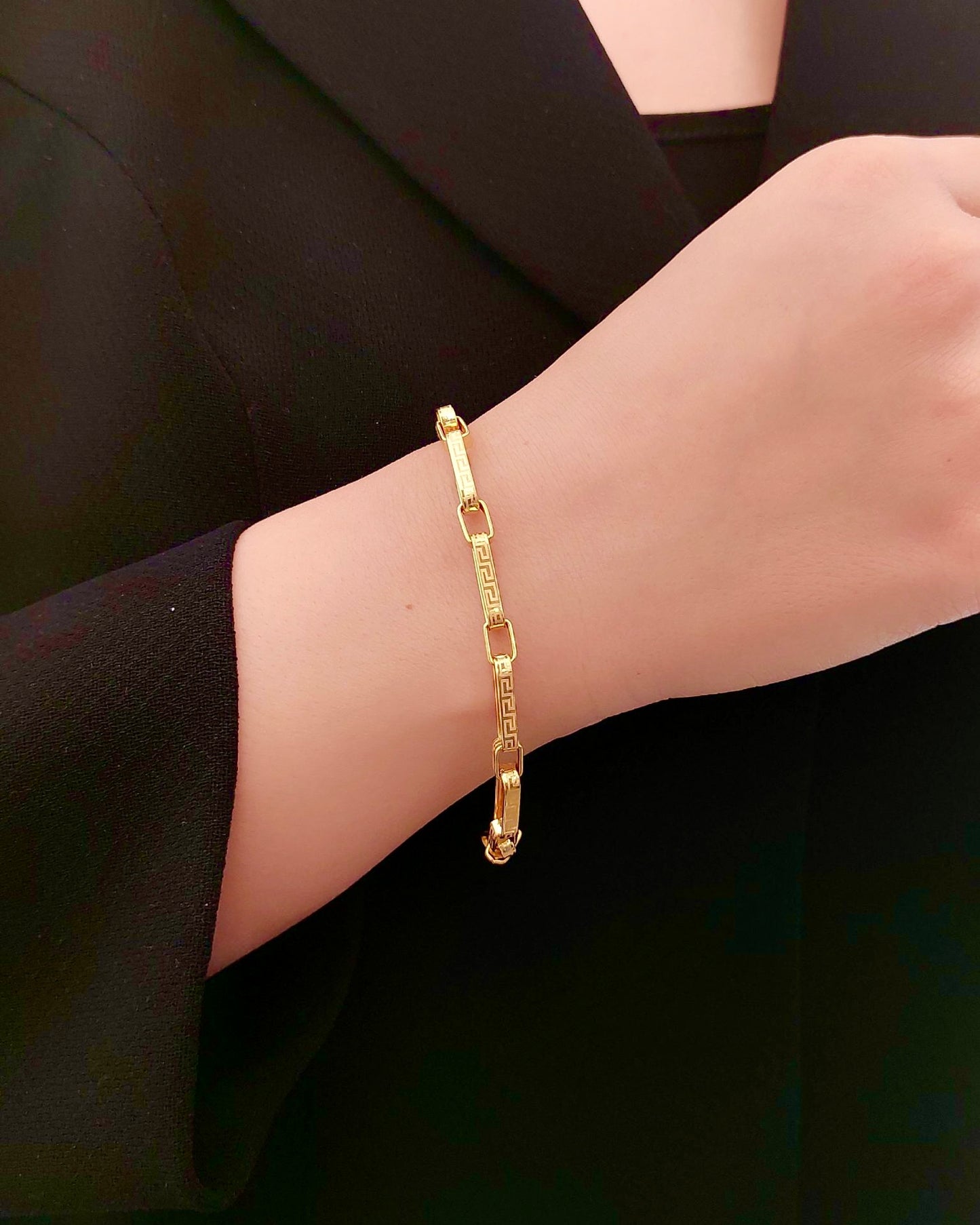 Armband aus 18 Karat Gelbgold mit geometrischem Gliederdesign und dezentem Muster, elegant am Handgelenk getragen und kombiniert mit einem schwarzen Outfit.
