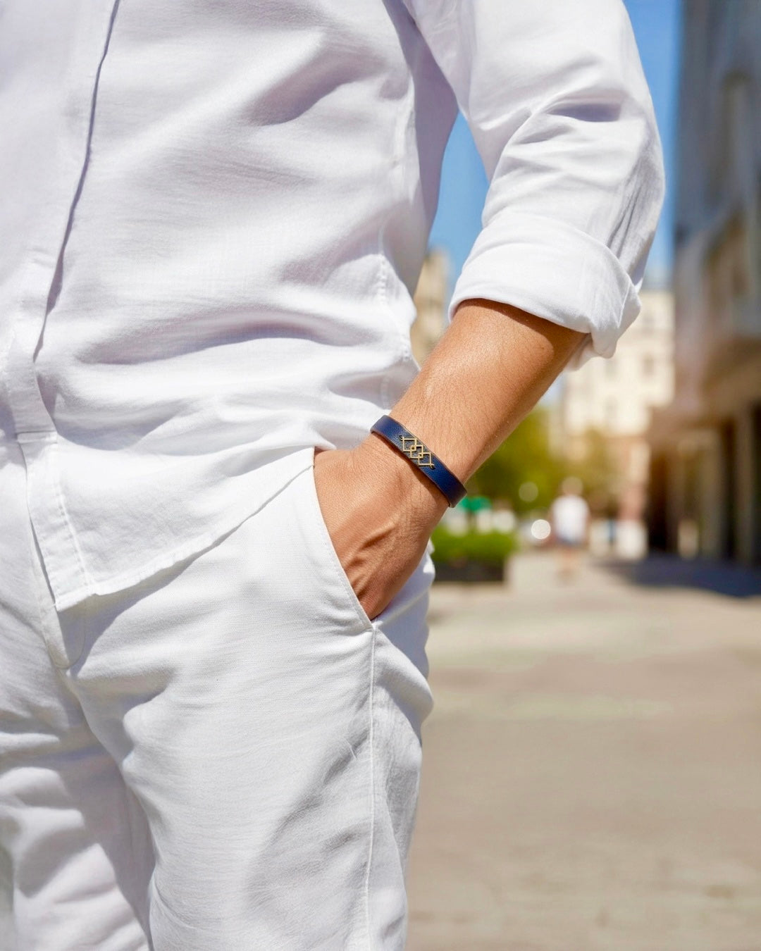 Elegantes Herrenarmband in Dunkelblau mit goldenem geometrischem Motiv, stilvoll getragen zu weißem Hemd und Hose in urbanem Sommerambiente.