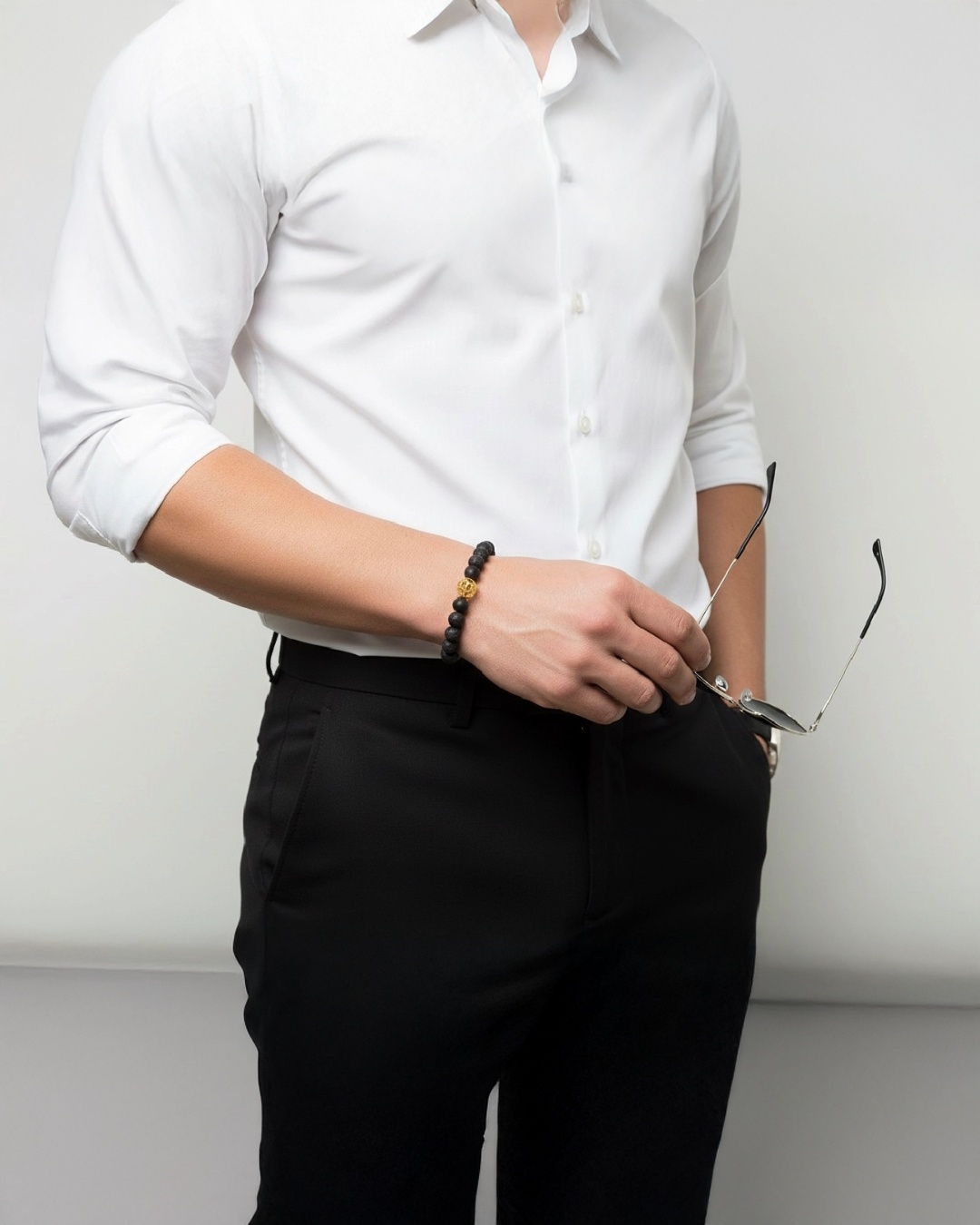 Elegantes Herrenarmband aus mattschwarzen Natursteinperlen mit goldfarbener Akzentperle, stilvoll kombiniert zu weißem Hemd und schwarzer Stoffhose – modernes Schmuckaccessoire für Business und Alltag.