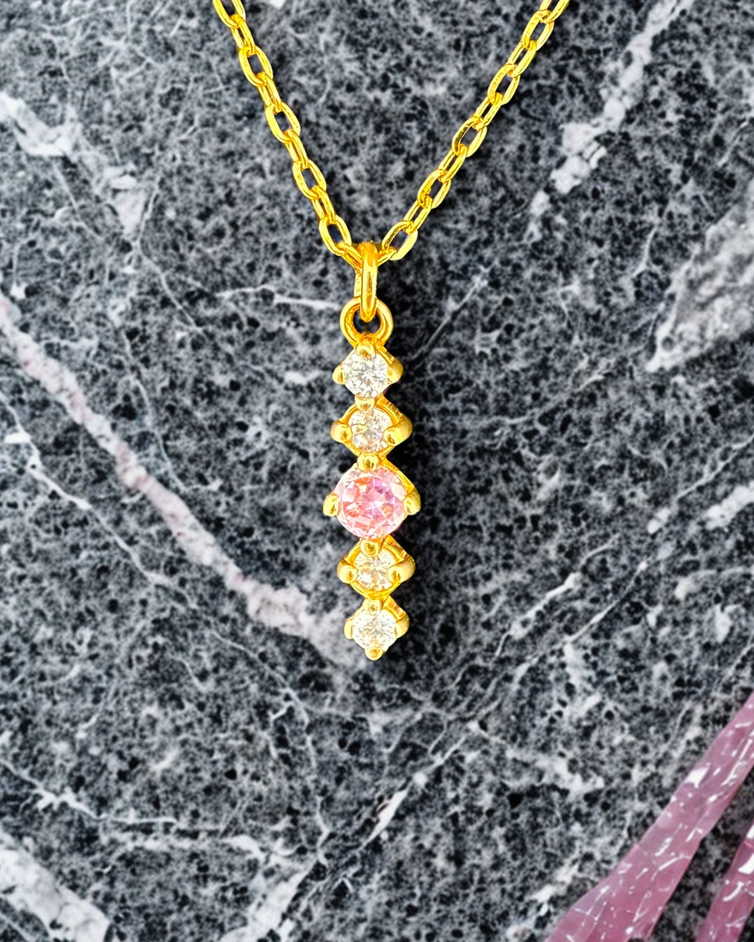Detailaufnahme einer 18k Goldkette mit Anhänger aus roséfarbenem und weißen Zirkonia auf Marmorhintergrund.