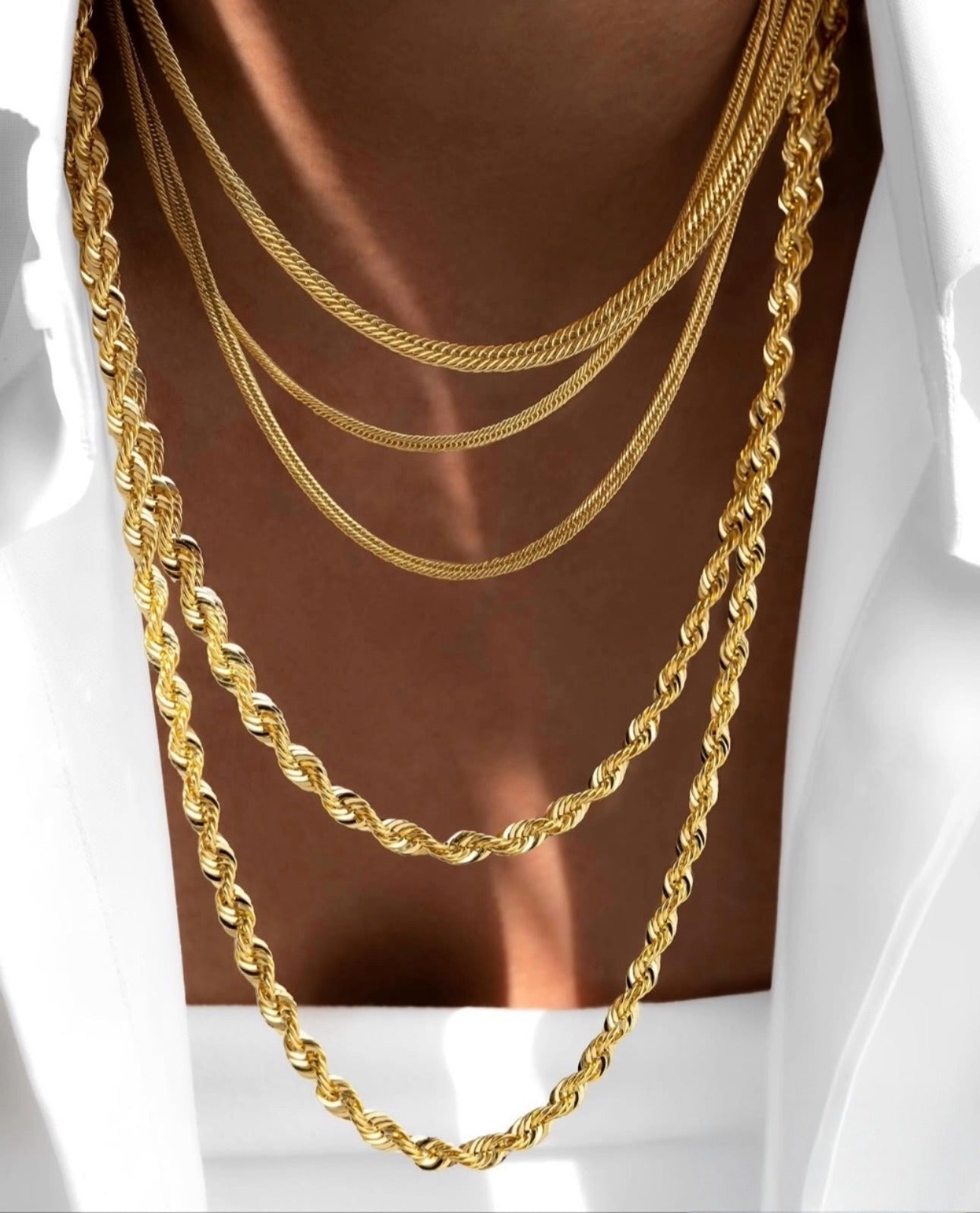 Mehrlagige 18k Gelbgold-Halsketten in verschiedenen Kettenstilen, elegant kombiniert auf gebräunter Haut, luxuriöser Goldschmuck mit feinem Glanz.