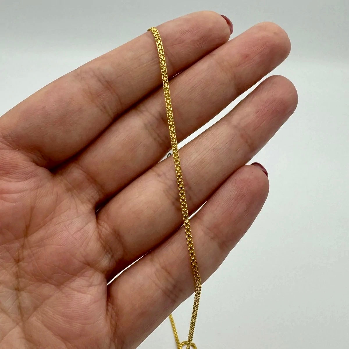 Nahaufnahme einer Bismarck-Kette aus 18k Gelbgold, die locker über die geöffnete Hand gelegt ist. Die flachen, dicht aneinanderliegenden Glieder reflektieren das Licht gleichmäßig und verleihen der Kette einen eleganten, geschmeidigen Glanz. Hintergrund neutral in hellem Weiß gehalten.