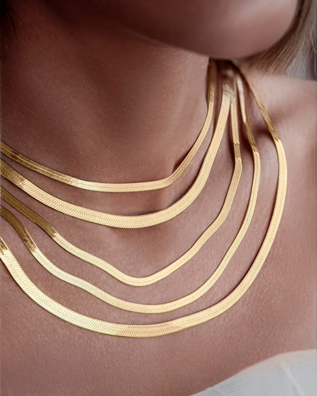 Mehrere übereinander getragene Fischgrätenketten aus 18k Gelbgold in unterschiedlichen Breiten, elegant am Hals drapiert und mit seidigem Glanz.