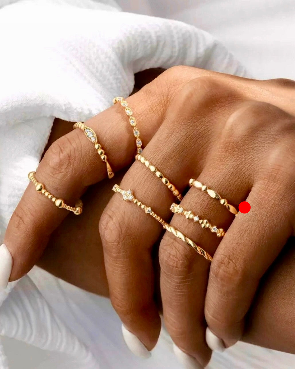 Lifestylebild: Hand mit mehreren feinen Ringen aus 18k Gold, teilweise mit Zirkonia Steinen besetzt. Verschiedene Designs: Kugelstruktur, glatte Oberflächen, zarte Fassungen.