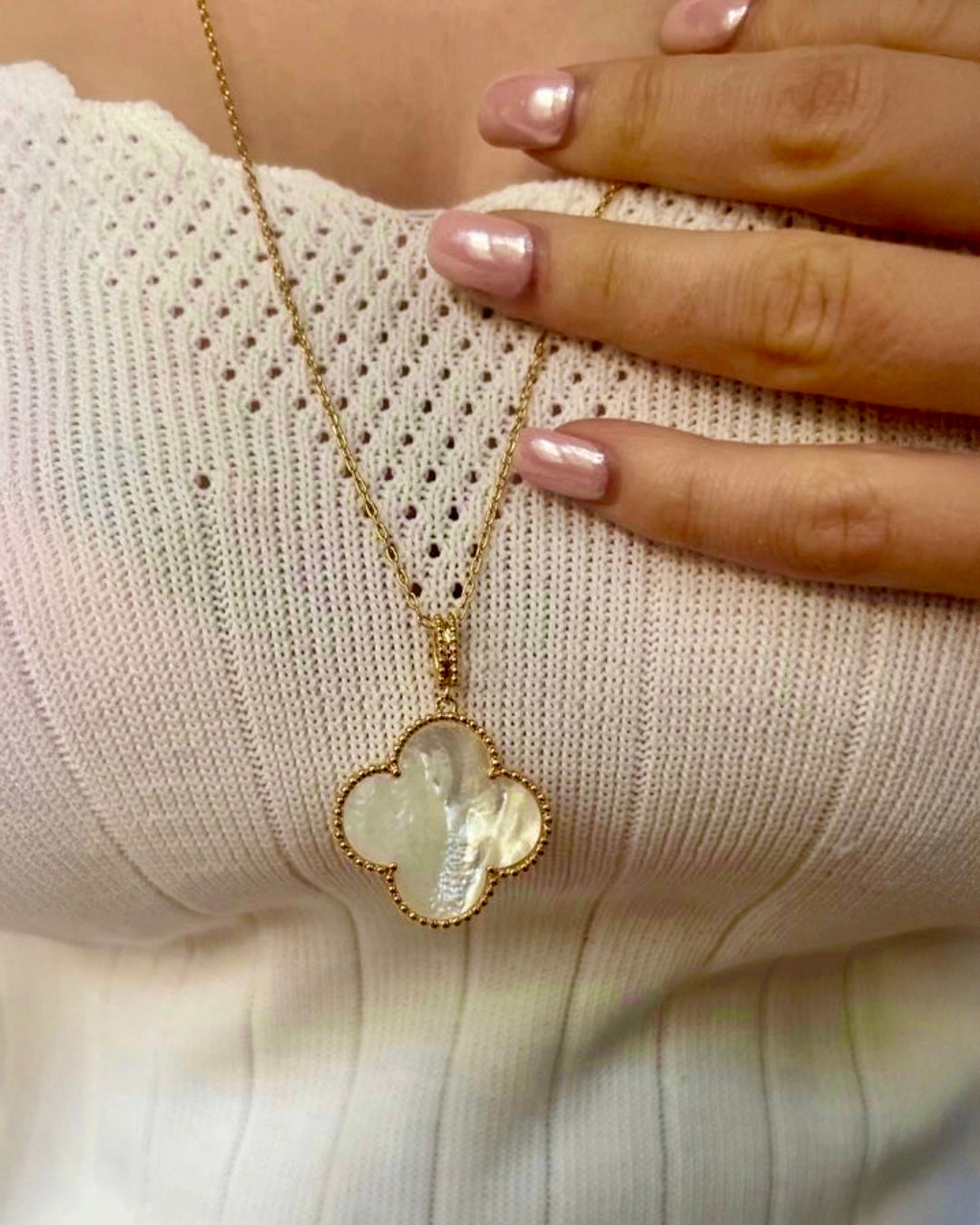18k Gelbgold-Halskette mit kleeblattförmigem Anhänger aus schimmerndem Perlmutt, filigrane Goldfassung, getragen am Dekolleté, elegante Damenkette in Nahaufnahme.
