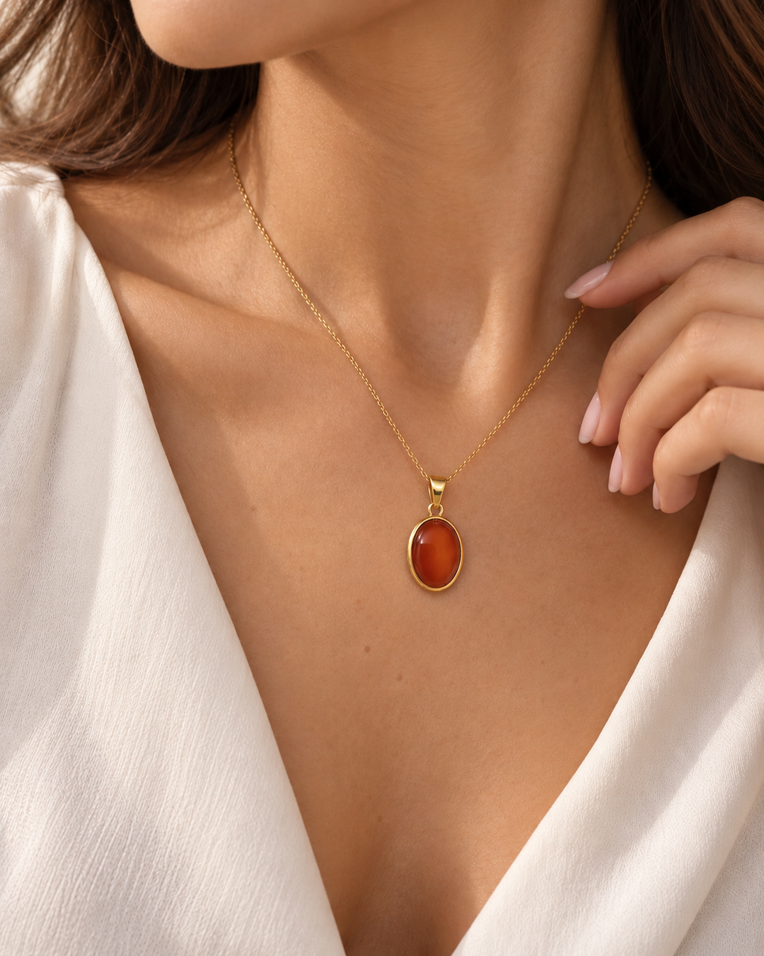 Ovaler Anhänger aus 18K Gelbgold mit rot-orangefarbenem Schmuckstein in goldener Fassung, getragen an einer feinen Goldkette am Dekolleté eines weiblichen Models.