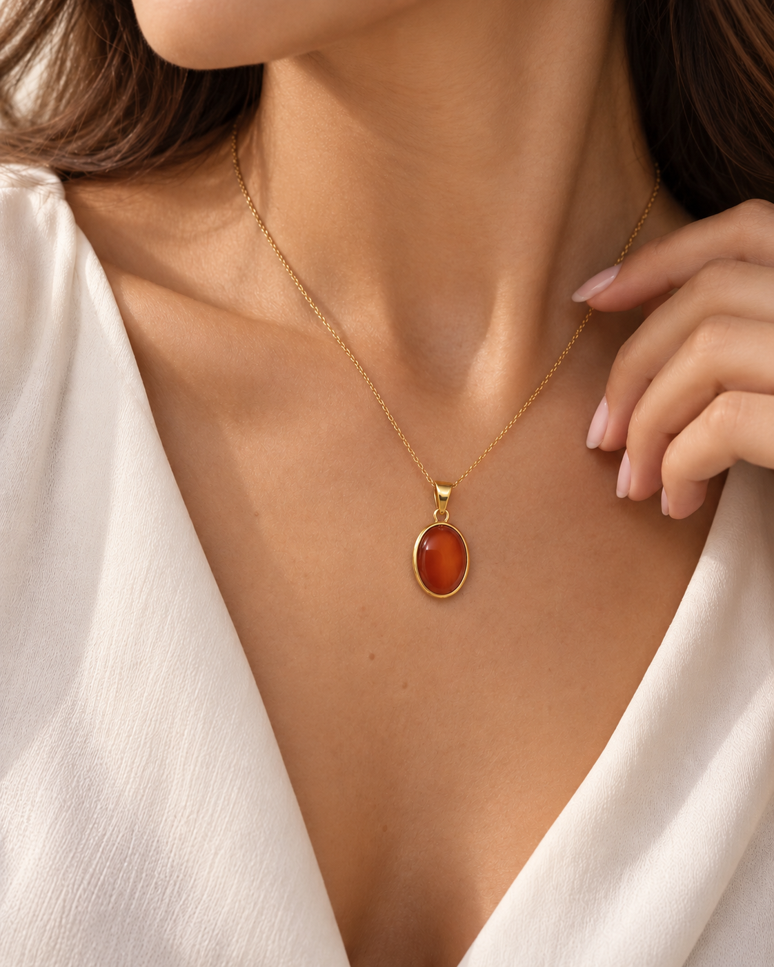 Ovaler Anhänger aus 18K Gelbgold mit rot-orangefarbenem Schmuckstein in goldener Fassung, getragen an einer feinen Goldkette am Dekolleté eines weiblichen Models.