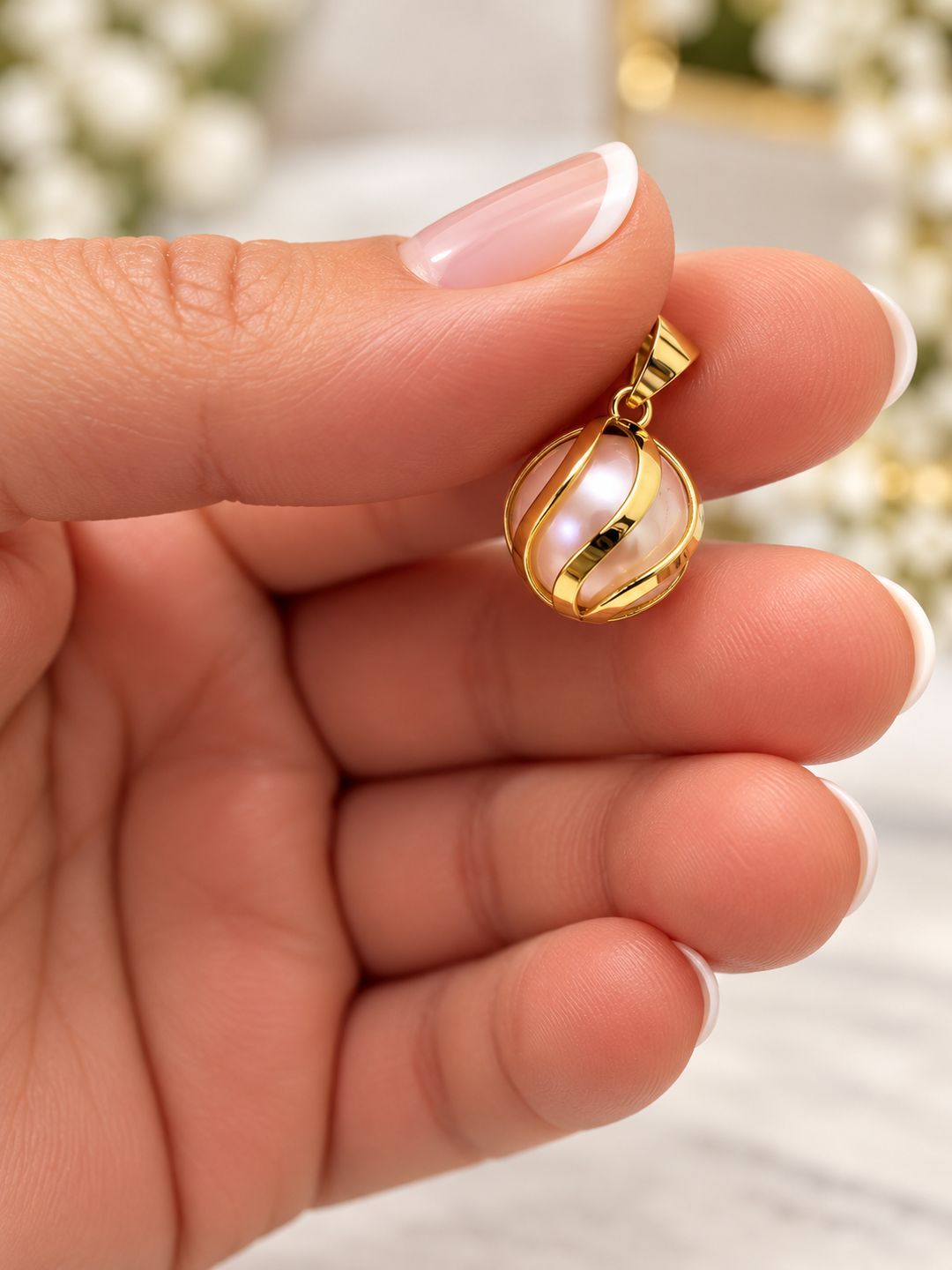 Shokoufeh Anhänger mit rosafarbener Kunstperle in geschwungener 18K Gelbgoldfassung, zwischen den Fingerspitzen gehalten.