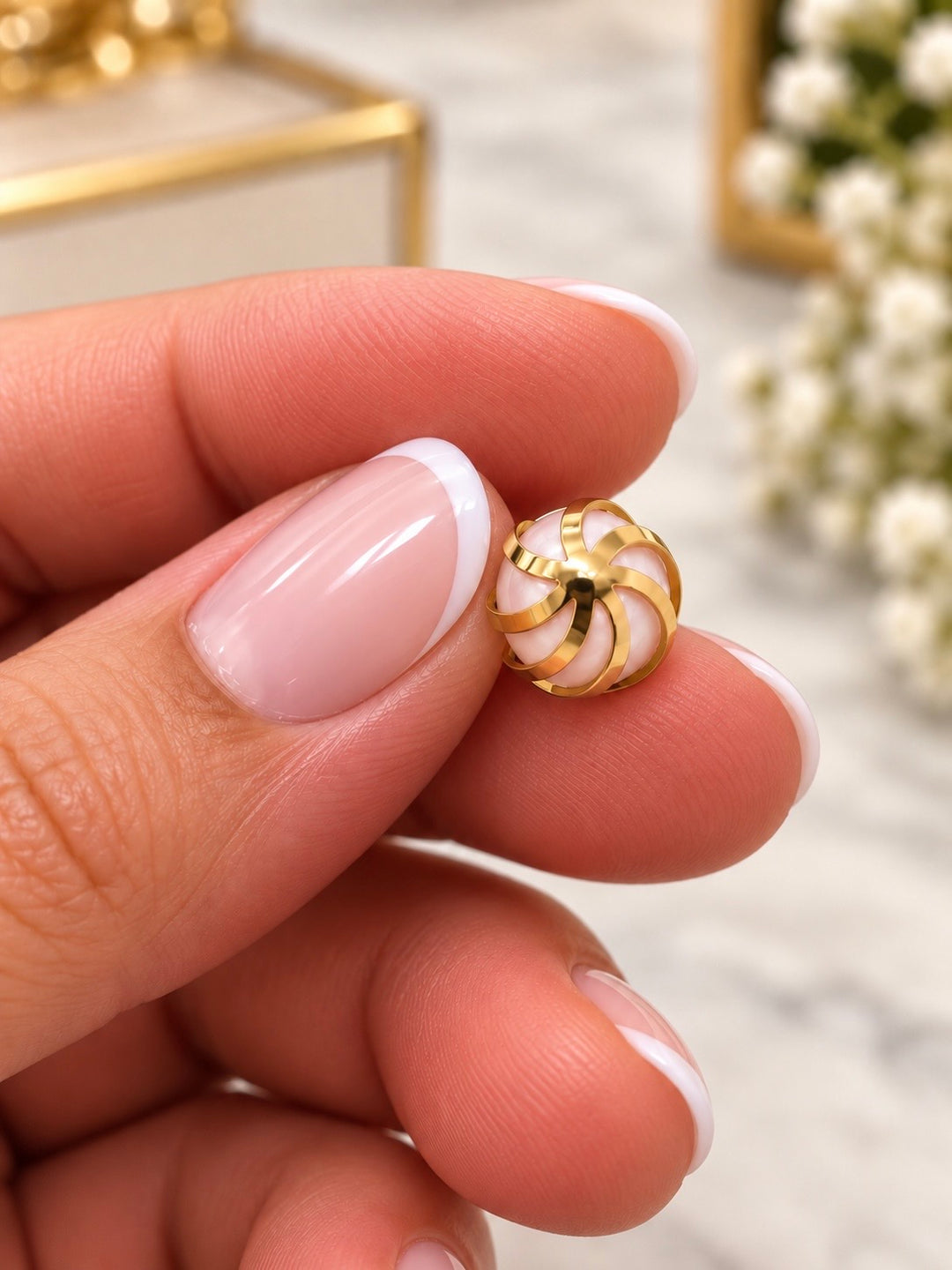 Shokoufeh Anhänger aus 18K Gelbgold mit rosafarbener Kunstperle und geschwungenen Goldbändern, zwischen zwei Fingern gehalten.