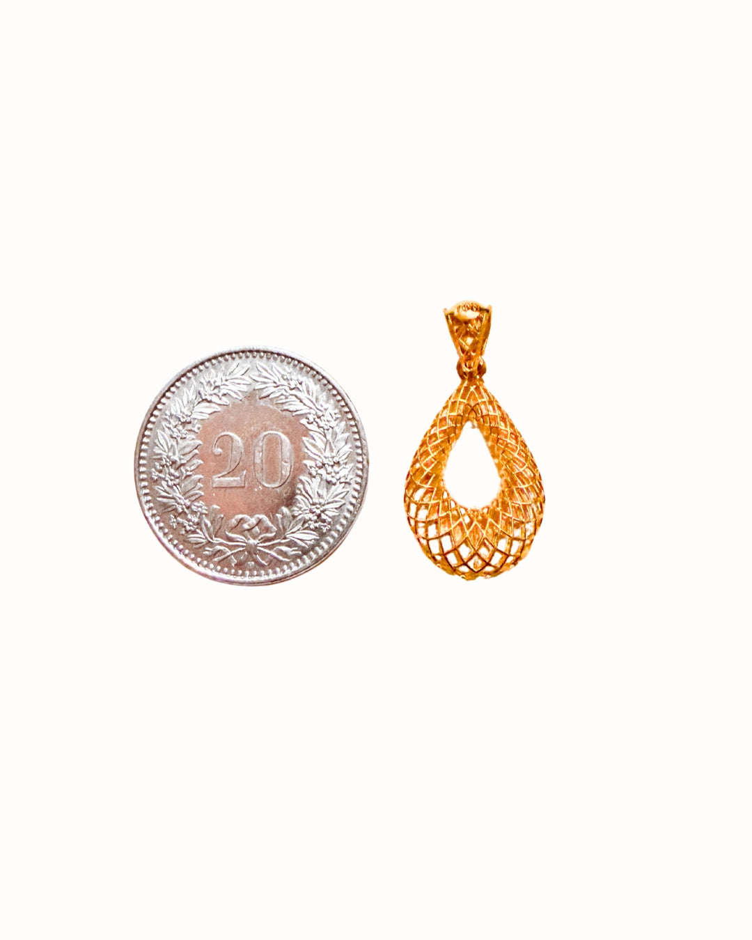 Anhänger aus 18k Gelbgold im Tropfen-Design neben einer 20-Rappen-Münze – Grössenvergleich des Modells Ghatreh-ye Mushabbak (Tropfen aus Spitze). Zeigt reale Proportionen des Schmuckstücks.