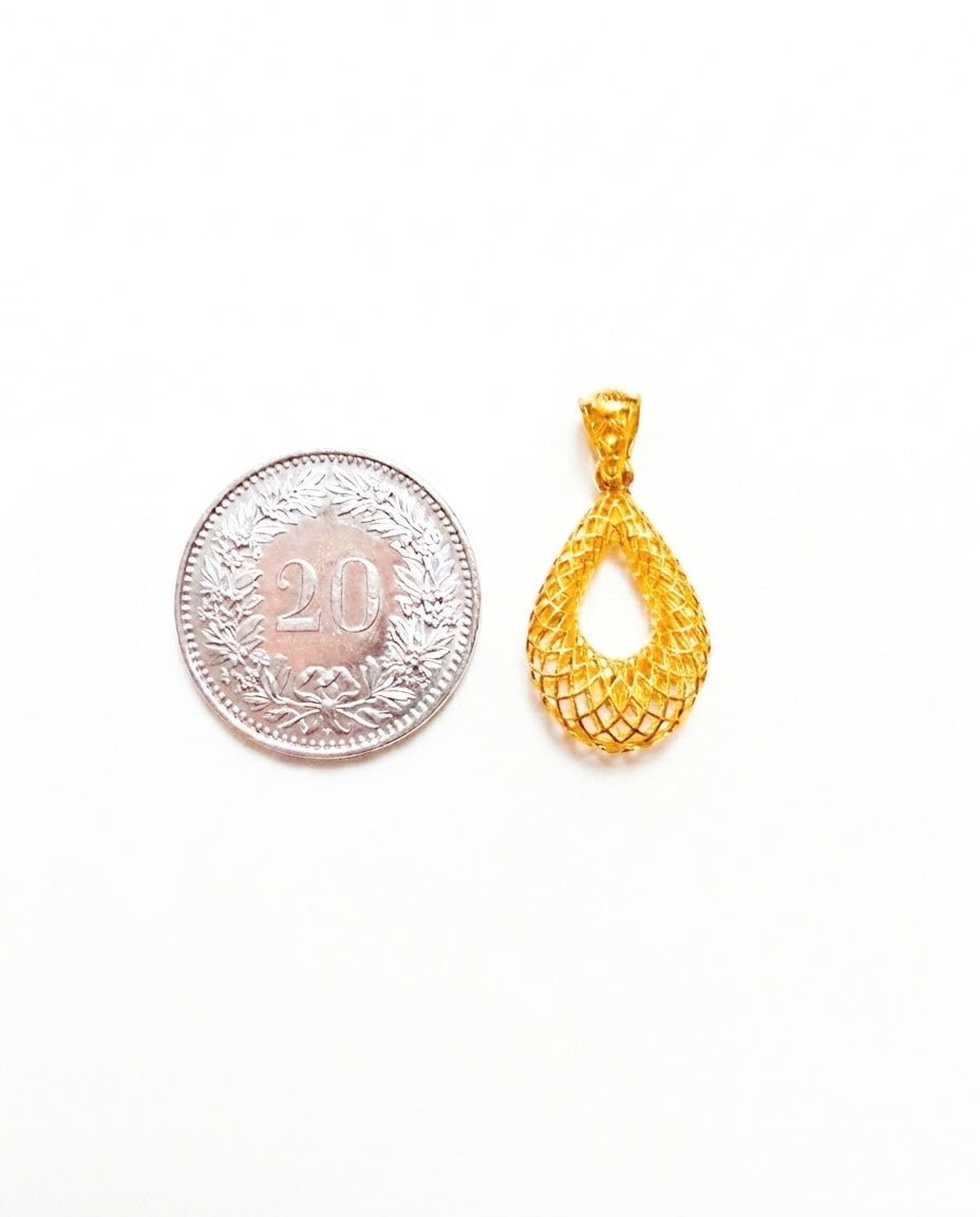 Filigraner Anhänger aus 18 Karat Gelbgold im tropfenförmigen Flechtdesign neben einer Schweizer 20-Rappen-Münze zum Grössenvergleich. Das offene, kunstvoll verflochtene Muster verleiht dem eleganten Goldanhänger eine leichte, luftige Optik und spiegelt traditionelle persische Goldschmiedekunst wider. Fotografiert auf weissem Hintergrund.