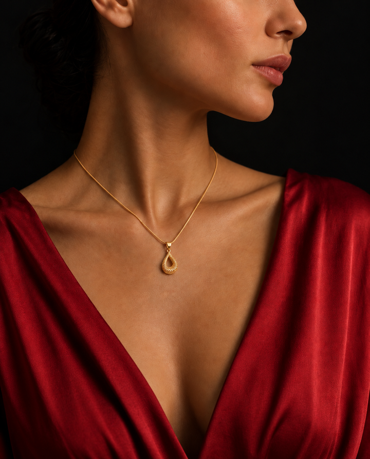 Elegante Frau trägt einen filigranen Anhänger aus 18 Karat Gelbgold im tropfenförmigen Flechtdesign an einer feinen Goldkette. Das kunstvoll gefertigte Schmuckstück liegt harmonisch auf dem Dekolleté und wird durch ein bordeauxrotes Kleid sowie einen dunklen Hintergrund stilvoll in Szene gesetzt. Luxuriöser Damenschmuck mit persischer Handwerkskunst für zeitlose Eleganz.