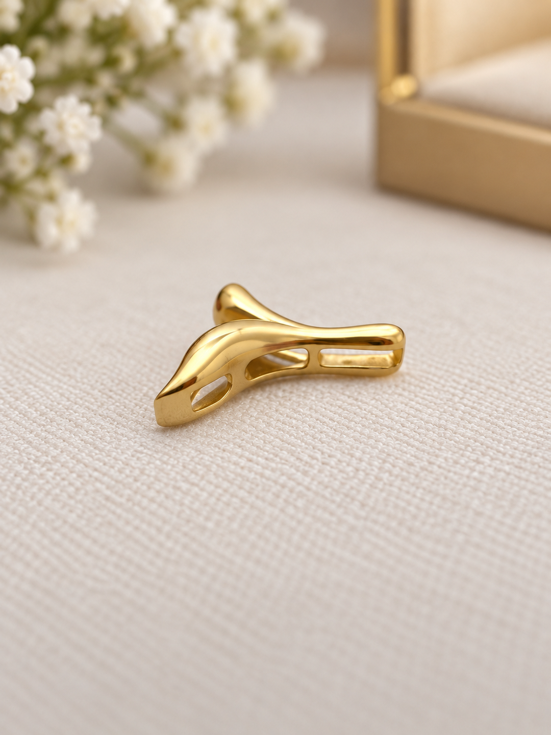 Detailaufnahme eines Anhängers in Form einer stilisierten Walflosse aus 18 Karat Gelbgold (750), mit glänzender, geschwungener Oberfläche und feinen Aussparungen, auf cremefarbenem Stoff präsentiert.