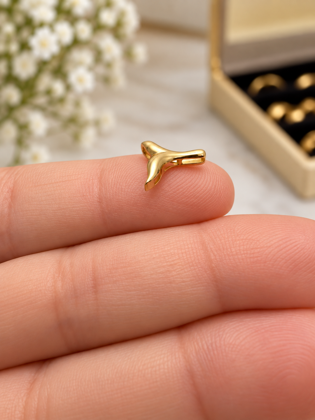 Seitenansicht eines Anhängers in Form einer stilisierten Walflosse aus 18 Karat Gelbgold (750), mit glänzender Oberfläche, auf einer Fingerspitze präsentiert.