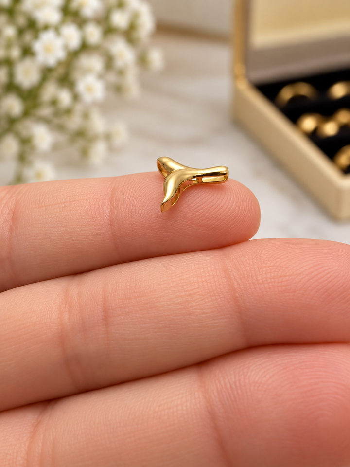 Seitenansicht eines Anhängers in Form einer stilisierten Walflosse aus 18 Karat Gelbgold (750), mit glänzender Oberfläche, auf einer Fingerspitze präsentiert.