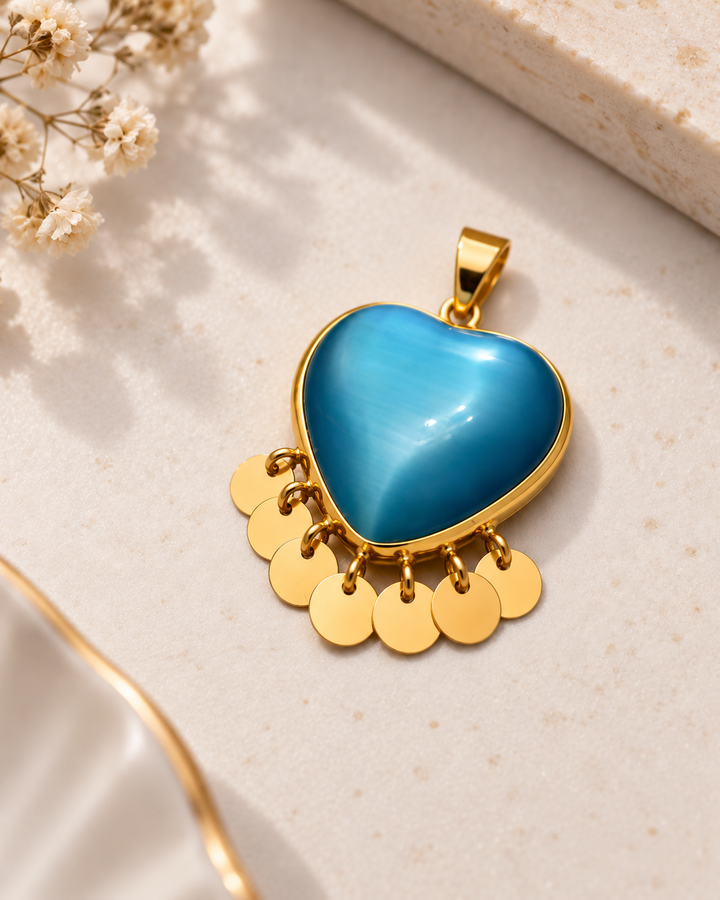 Herzförmiger Anhänger aus Gelbgold mit blau schimmerndem Stein und sieben beweglichen Goldplättchen auf hellem, elegantem Hintergrund.