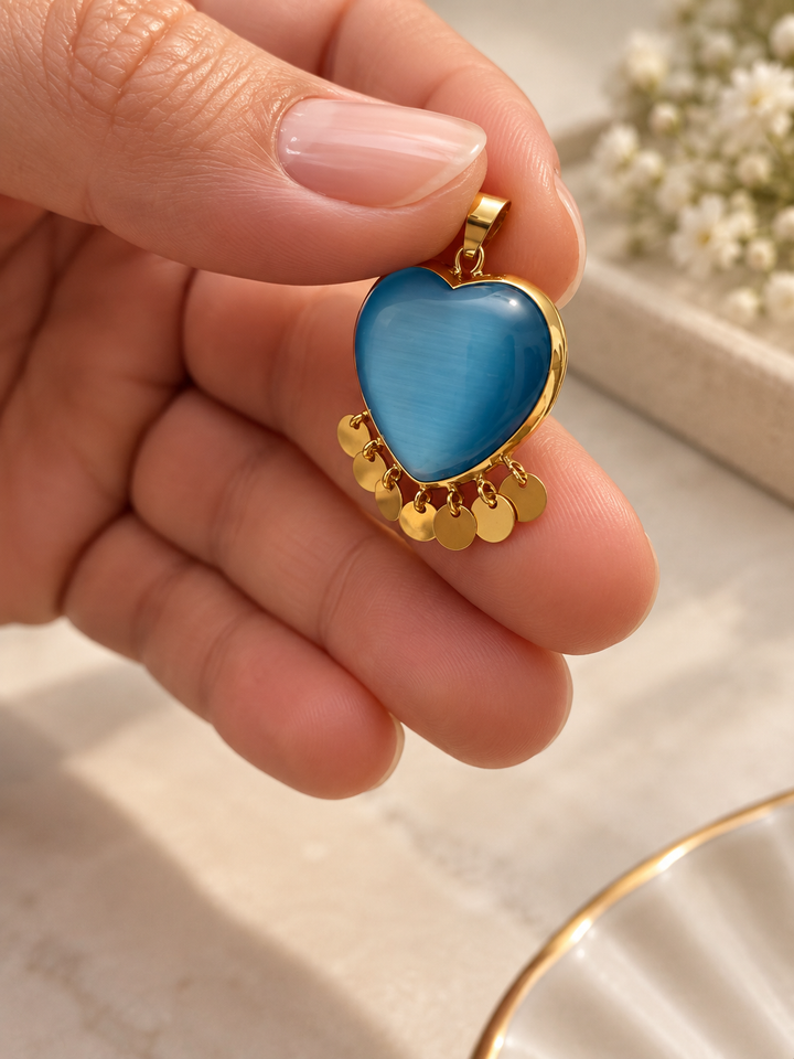 Herzförmiger Anhänger aus Gelbgold mit blau schimmerndem Stein und sieben beweglichen Goldplättchen, elegant in der Hand präsentiert.