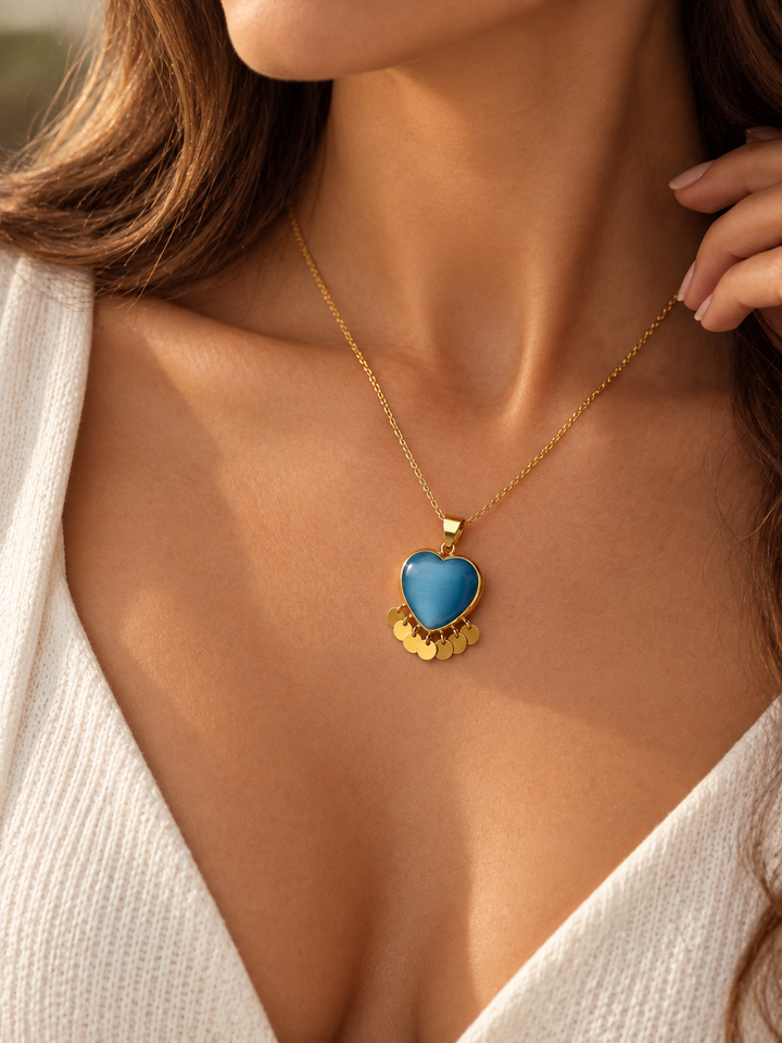 Model trägt einen herzförmigen Anhänger aus Gelbgold mit blau schimmerndem Stein und sieben beweglichen Goldplättchen an einer feinen Goldkette.