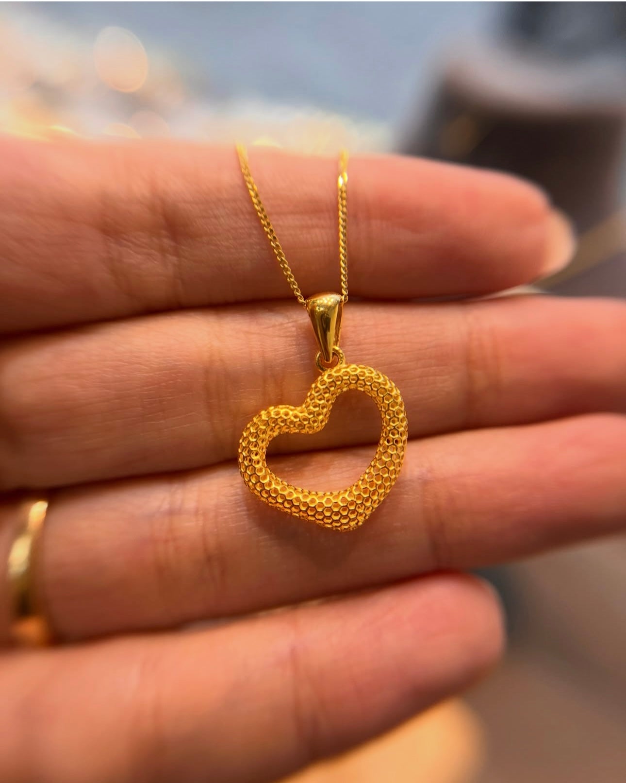 Herzanhänger aus 18k Gelbgold auf Hand getragen – fein, authentisch & zeitlos.