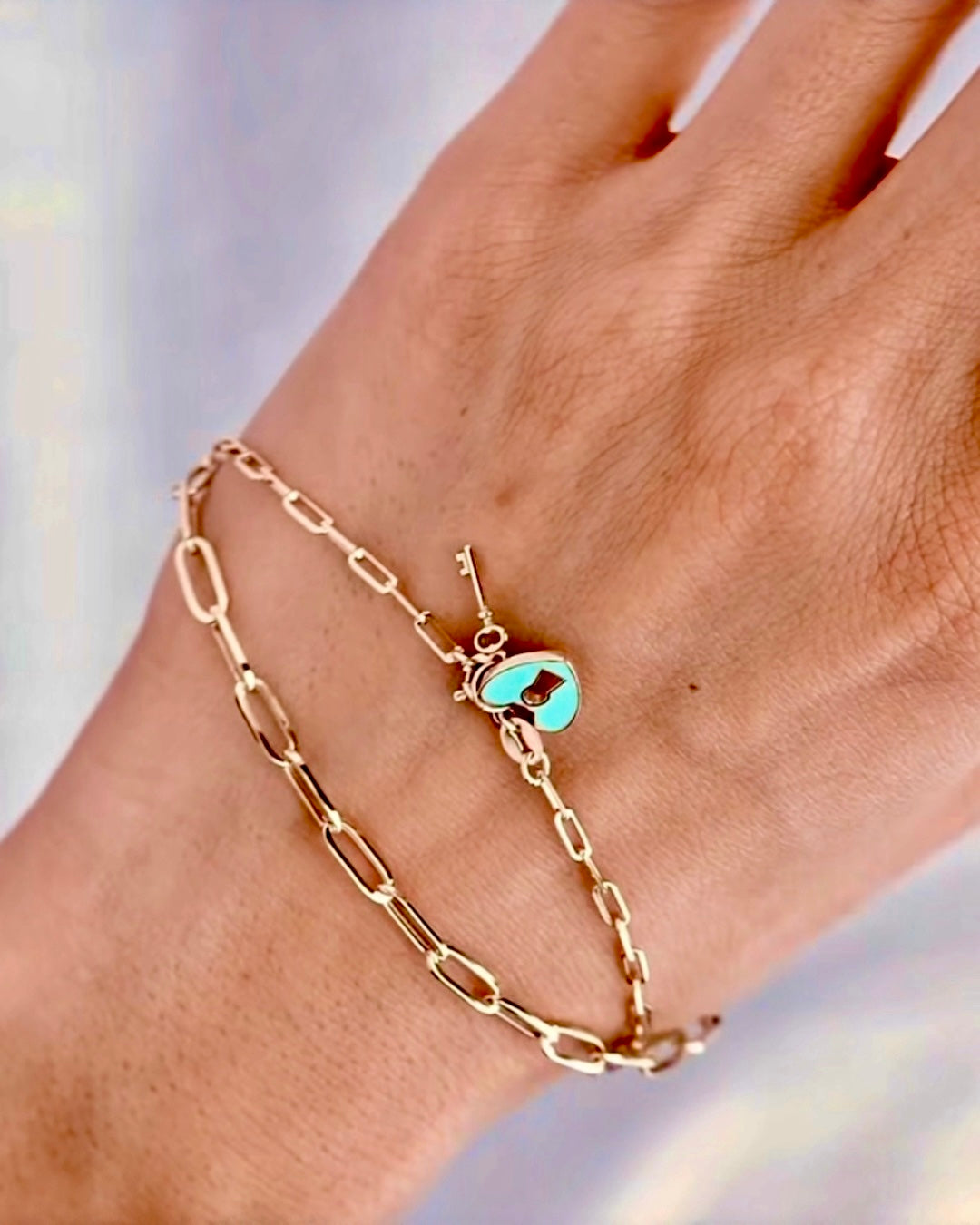 18k Gelbgold-Armband im Paperclip-Design am Handgelenk getragen, mit filigranem Herzverschluss in Türkis-Emaille und kleinem Schlüsselanhänger, elegant und modern inszeniert.