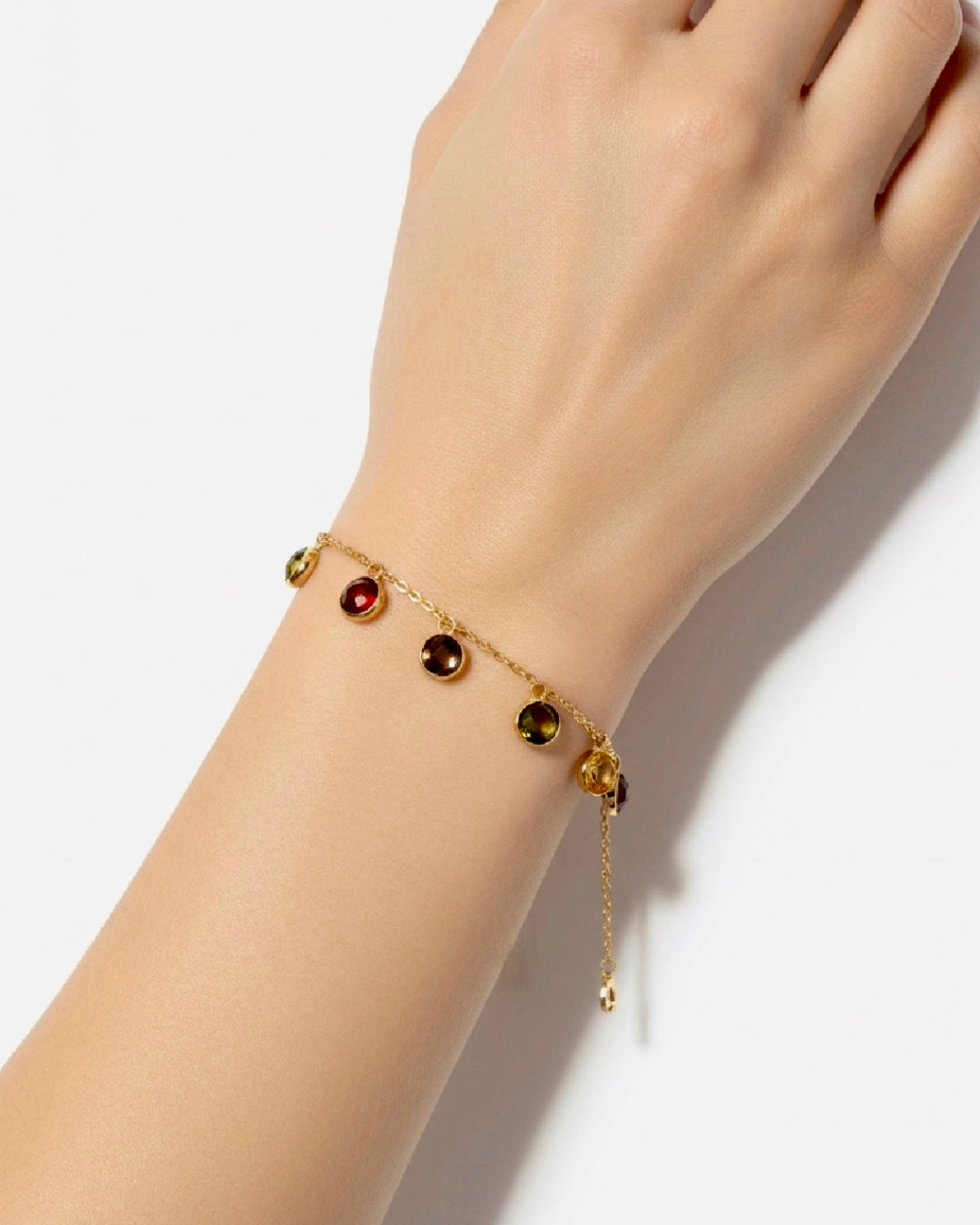 Elegantes Armband aus 18k Gelbgold mit feiner Kette und mehreren runden, farbigen Edelstein-Anhängern in Rot-, Grün- und Goldtönen, getragen am Handgelenk einer Frau.
