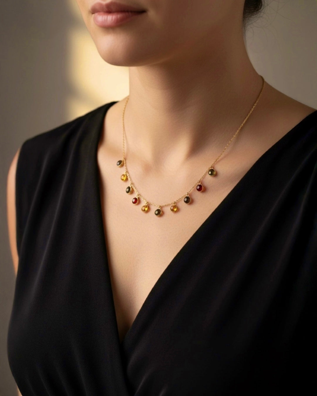 Elegante 18k Gelbgold-Halskette mit feiner Kette und mehreren kleinen, runden Anhängern aus farbigen Edelsteinen in Rot-, Grün- und Goldtönen, getragen von einer Frau in schwarzem Kleid.