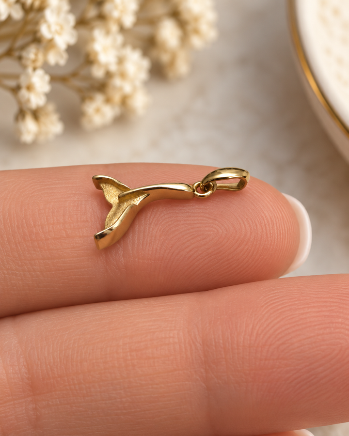 Detailansicht des Dom-e Val Anhängers aus 18k Gelbgold in Form einer Walflosse auf der Hand