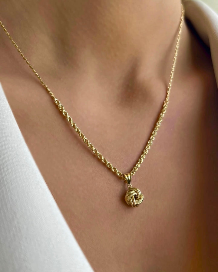 Elegante Halskette aus 18 Karat Gelbgold mit feiner gedrehter Kordelkette und kleinem Knoten-Anhänger. Der filigrane Anhänger mit strukturierter Oberfläche symbolisiert Verbundenheit und Beständigkeit. Getragen auf dem Dekolleté einer Frau, kommt der warme Goldglanz besonders edel zur Geltung. Perfekt für einen zeitlosen, stilvollen Look.