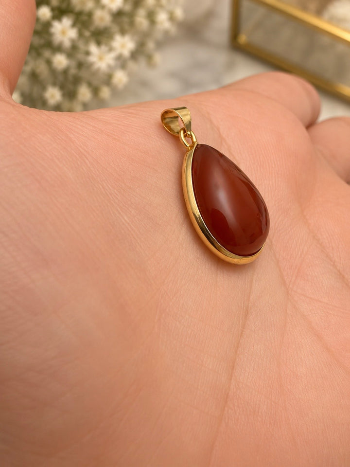 Roter Tropfenanhänger aus 18k Gelbgold mit synthetischem Schmuckstein, auf einem Handrücken präsentiert.