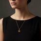 Elegante Frau mit schwarzem Outfit trägt feine 18k Gelbgold-Halskette mit filigranem, tropfenförmigem Anhänger in modernem, minimalistischen Design.