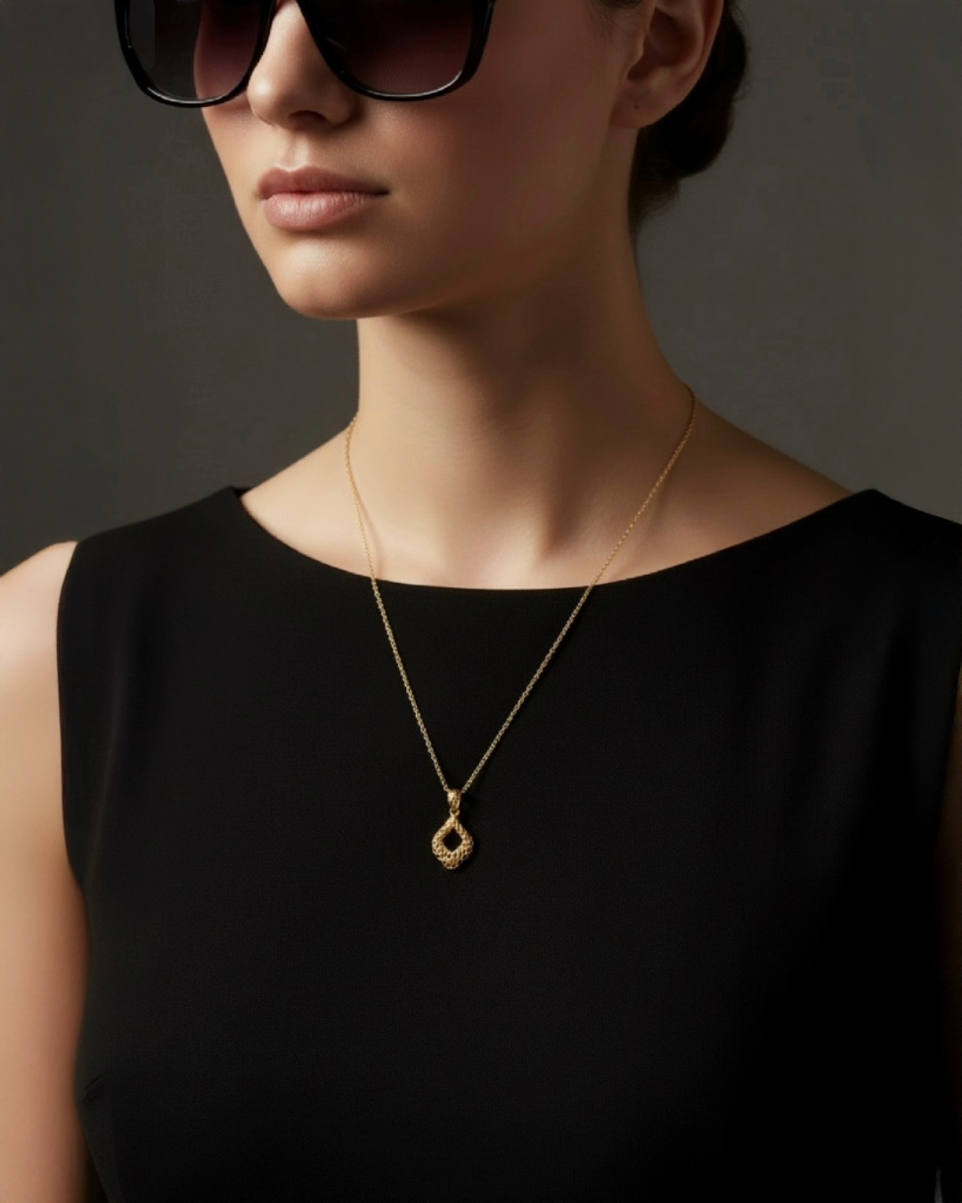 Elegante Frau mit schwarzem Outfit trägt feine 18k Gelbgold-Halskette mit filigranem, tropfenförmigem Anhänger in modernem, minimalistischen Design.