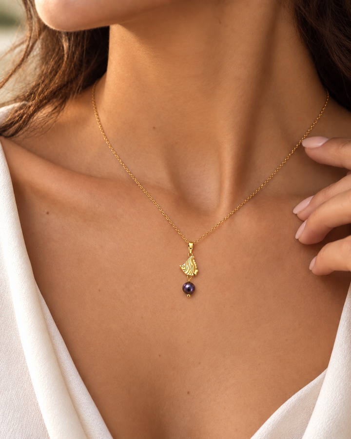 Nahaufnahme eines Models mit filigraner Halskette und Fisch-Anhänger aus 18k Gelbgold, verziert mit einer dunkelvioletten Zuchtperle.