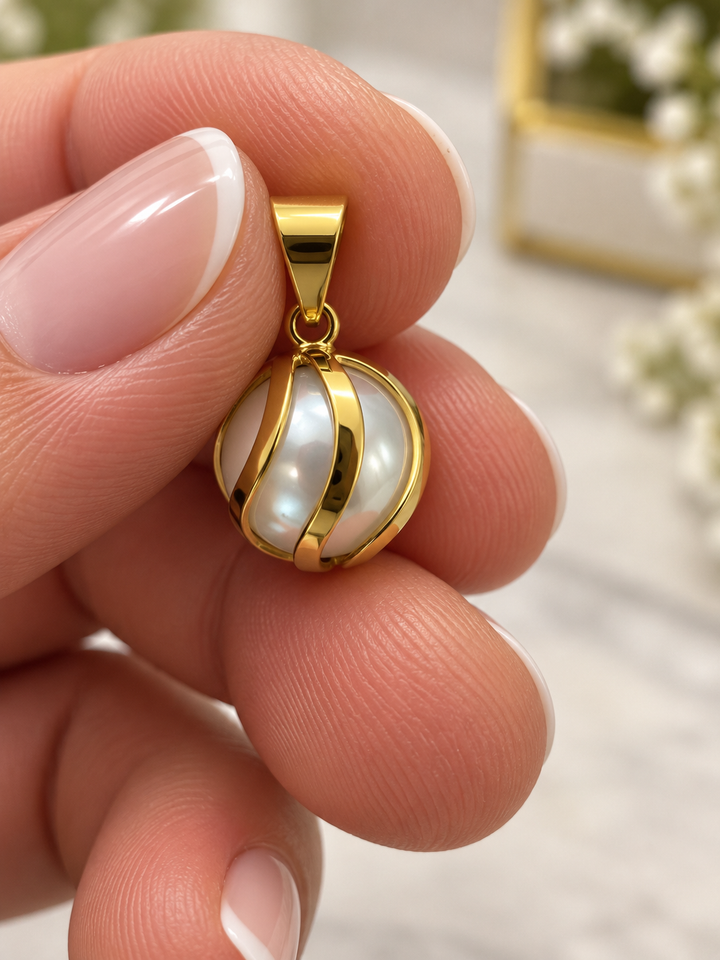 Makroaufnahme des Anhängers zwischen zwei Fingern mit sichtbarer Goldöse und schimmernder weisser Perle.