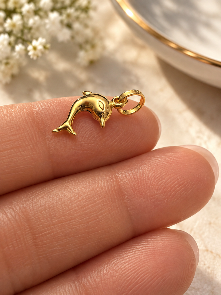 Filigraner Delfin-Anhänger aus glänzendem Gelbgold auf einer Hand, stilvoll inszeniert vor einem warmen, eleganten Hintergrund.