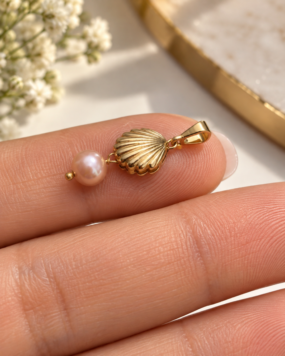 Detailansicht des Sadaf-o Morvarid Anhängers aus 18k Gelbgold mit gerippter Muschel und roséfarbener Zuchtperle auf der Hand