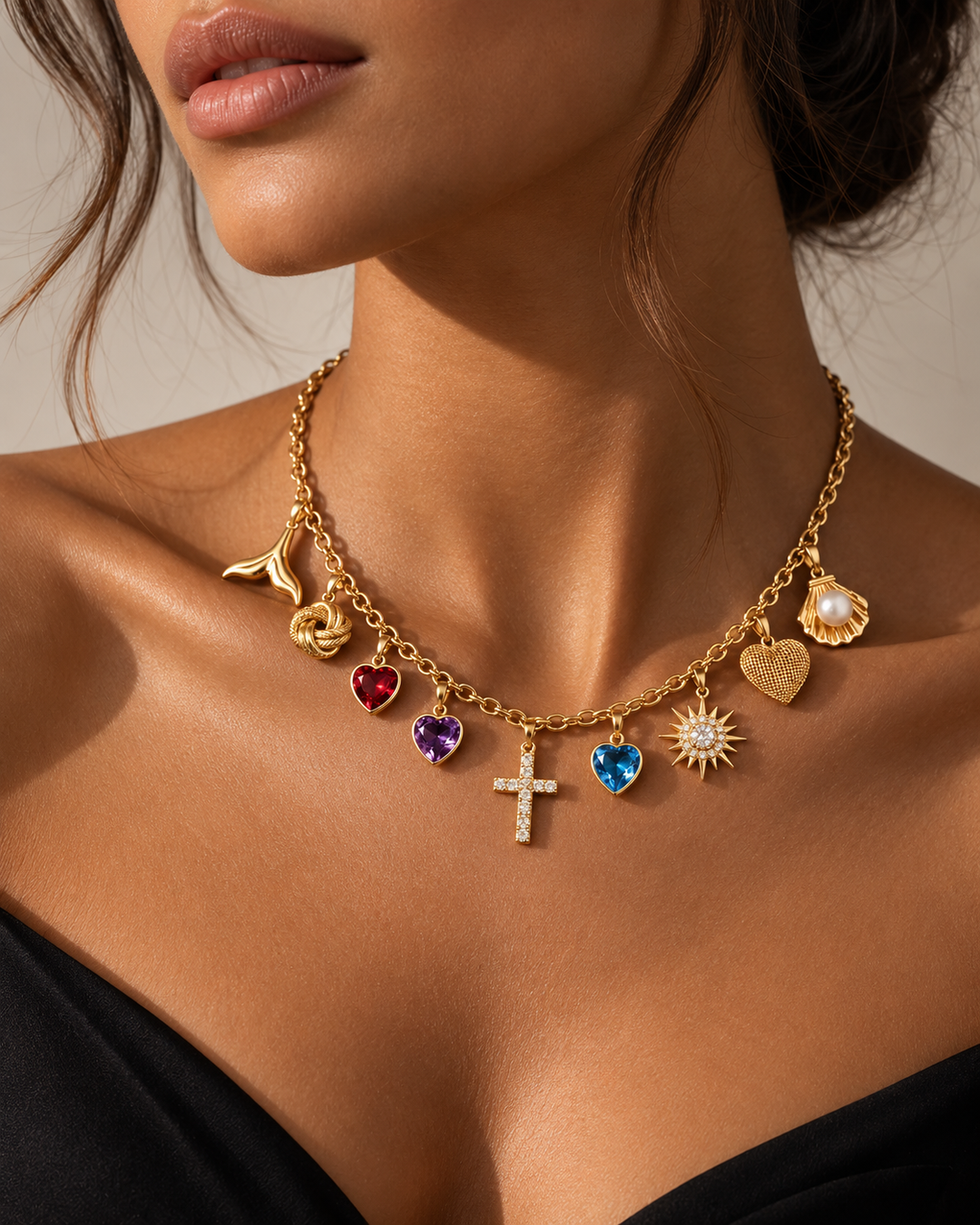 18 Karat Gold Charm-Halskette mit verschiedenen Anhängern an einem Model getragen. Die Kette kombiniert ein funkelndes Kreuz mit Zirkonia, Herzanhänger mit roten, violetten und blauen Edelstein-Optiken, eine Sonne mit Zirkonia, ein strukturiertes Goldherz, eine Muschel mit Perle, einen Knoten sowie einen Ast-Anhänger. Hochwertiger, eleganter Statement-Schmuck für Damen und Herren mit modernem, luxuriösem Design.