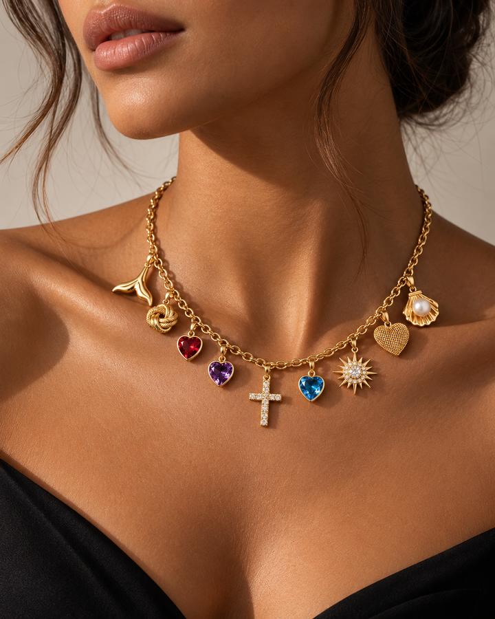 18 Karat Gold Charm-Halskette mit verschiedenen Anhängern an einem Model getragen. Die Kette kombiniert ein funkelndes Kreuz mit Zirkonia, Herzanhänger mit roten, violetten und blauen Edelstein-Optiken, eine Sonne mit Zirkonia, ein strukturiertes Goldherz, eine Muschel mit Perle, einen Knoten sowie einen Ast-Anhänger. Hochwertiger, eleganter Statement-Schmuck für Damen und Herren mit modernem, luxuriösem Design.