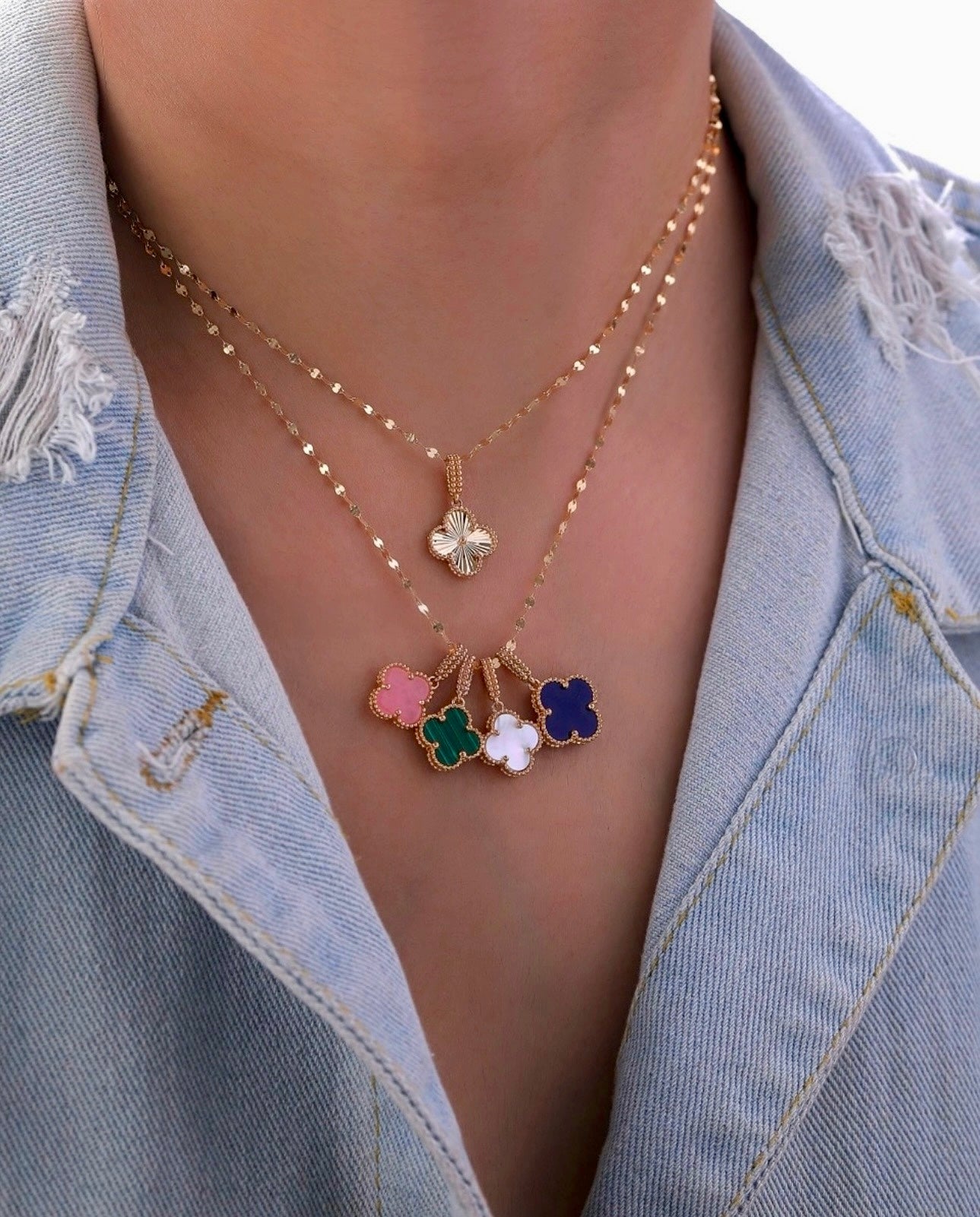 Nahaufnahme einer Halskette aus 18k Gelbgold mit kleeblattförmigem Anhänger in Weiß, getragen über einer offenen Jeansjacke.