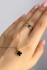 Feiner 18k Gelbgold-Anhänger in Kleeblattform mit schwarzem Inlay und perlenartigem Goldrand, an zarter Goldkette, dekorativ über einer Hand mit passendem Ring in Schwarz-Gold getragen.