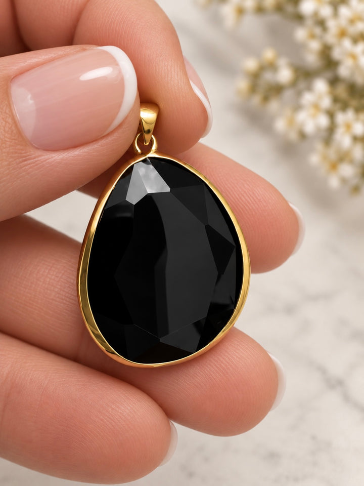 Tropfenförmiger schwarzer Anhänger aus 18k Gelbgold in der Hand gehalten