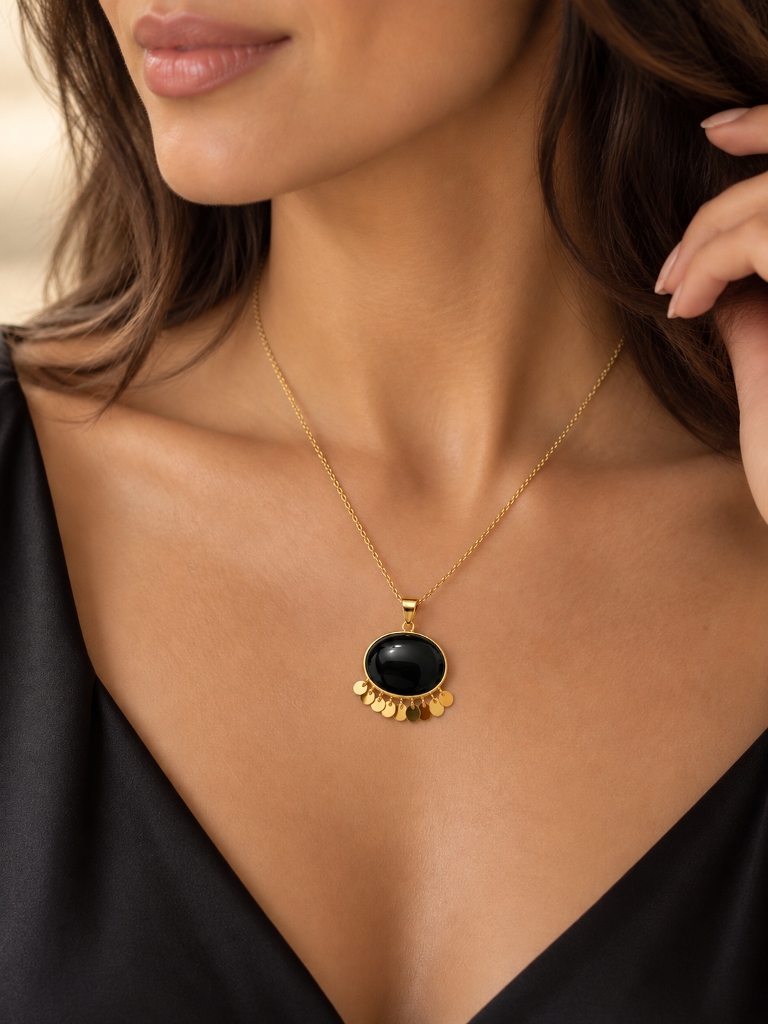 Elegante Halskette aus Gelbgold mit ovalem schwarzem Onyx-Anhänger und feinen, beweglichen Goldplättchen, getragen zu einem schwarzen Kleid.