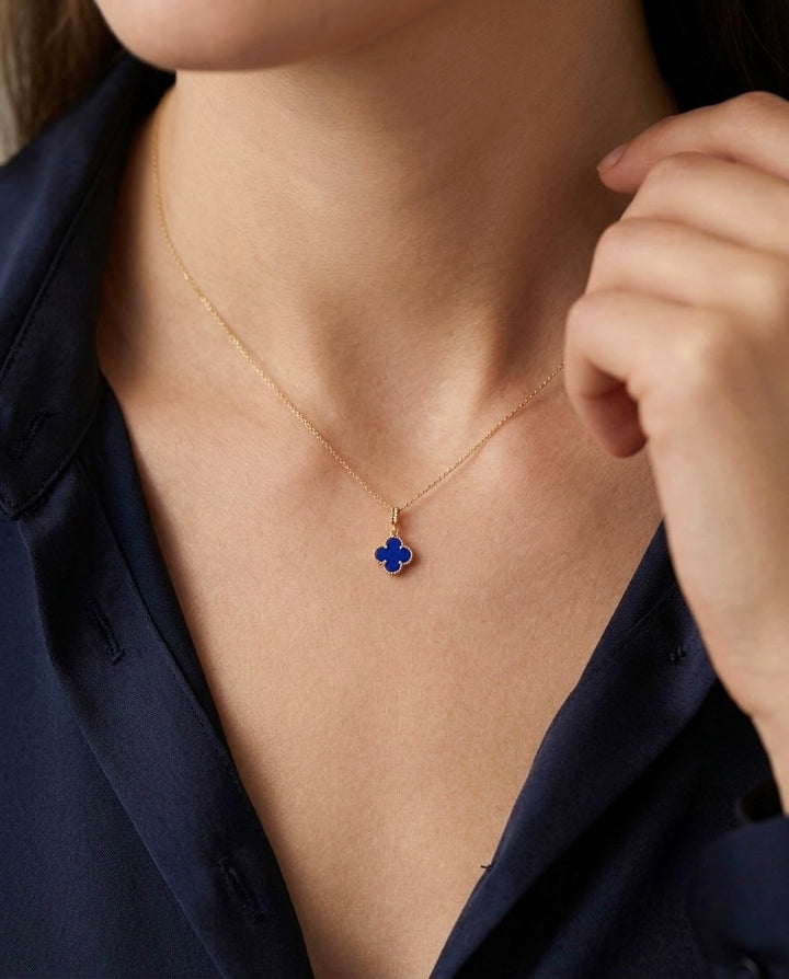 Nahaufnahme einer eleganten 18 Karat Gelbgold-Halskette mit filigraner Ankerkette und kleeblattförmigem Anhänger in tiefem Königsblau. Der Anhänger ist von einer feinen Goldfassung umgeben und wird dezent am Hals getragen. Zeitloser Goldschmuck für Damen – ideal als edles Geschenk oder für den Alltag.