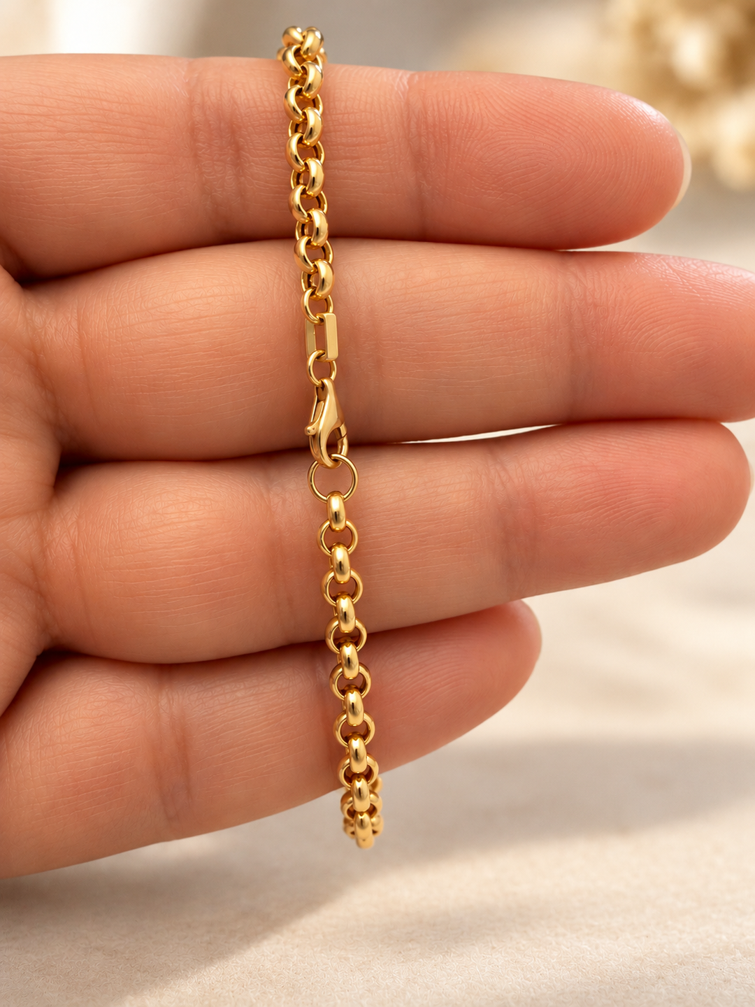 Nahaufnahme eines Rolo-Armbands aus 18 Karat Gelbgold mit hochglanzpolierten, ineinandergreifenden Erbskettengliedern auf einer Hand.