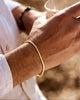 Feines, minimalistisches Armband aus 18k Gelbgold am Handgelenk eines Mannes, warmes Sonnenlicht, elegante Alltagsaufnahme mit natürlicher Hautstruktur und weichem Hintergrund.